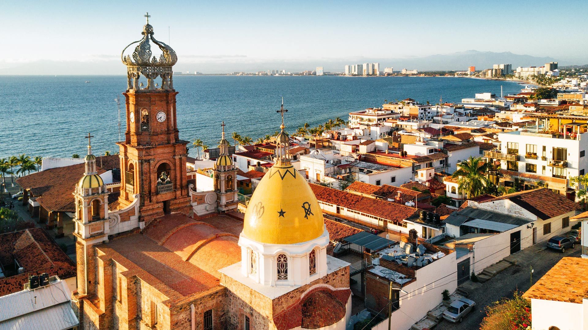 Una vista aérea de una ciudad con una iglesia en primer plano y el océano al fondo.