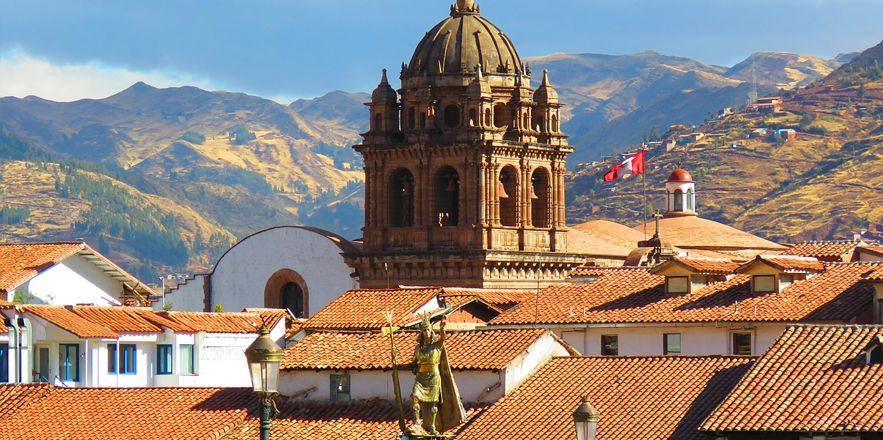 Una iglesia con una cúpula en la parte superior está en el medio de una ciudad con montañas al fondo.