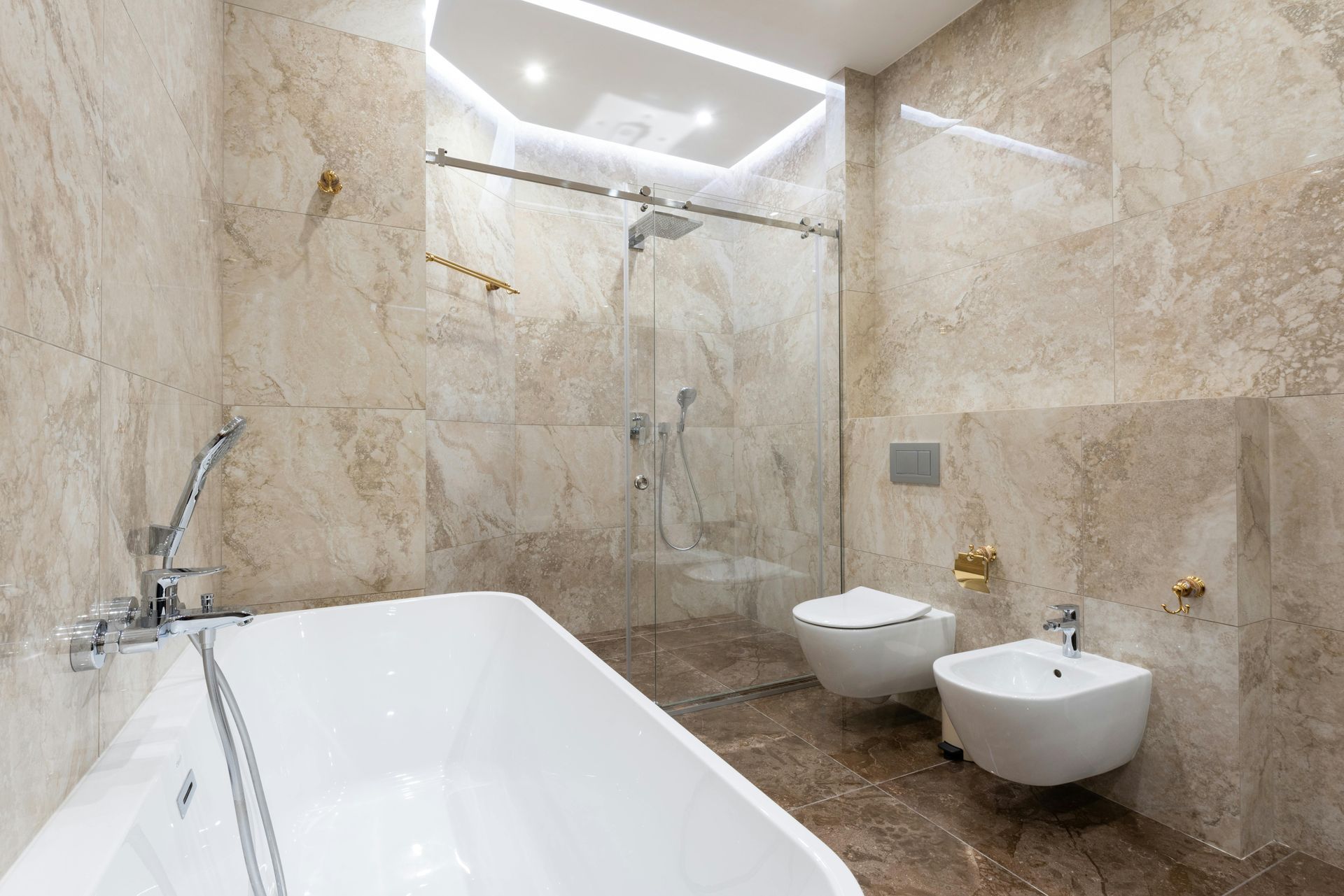 Luxurious beige tiled bathroom with tub, shower, and floating toilet and bidet.