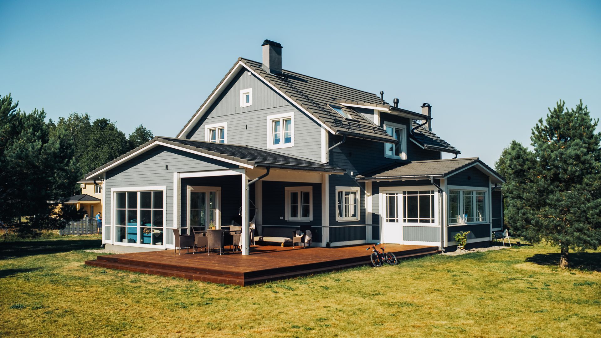 A large house with a large deck in the middle of a lush green field.