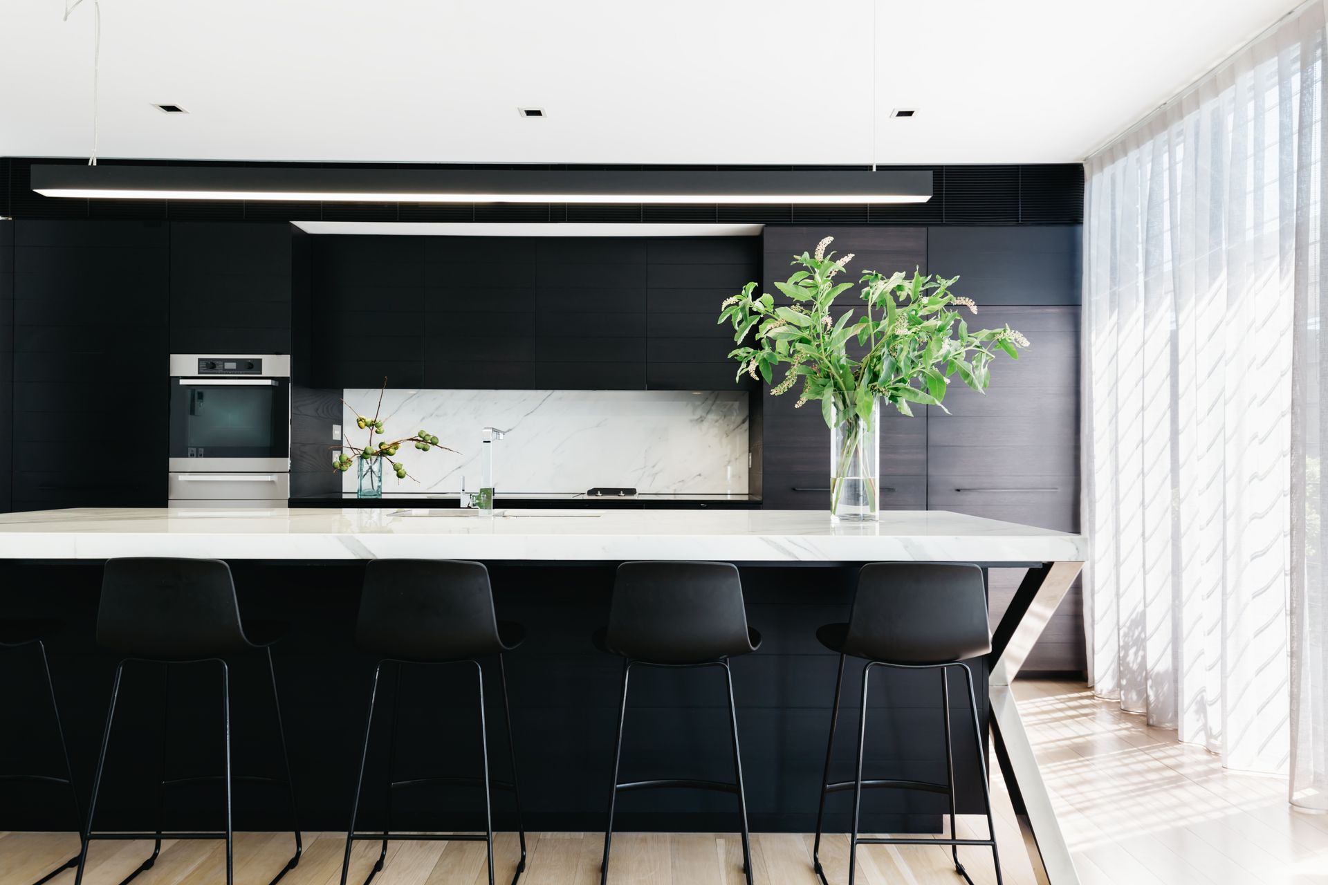 View of a black kitchen with marble-looking laminate benchtop and high chairs.