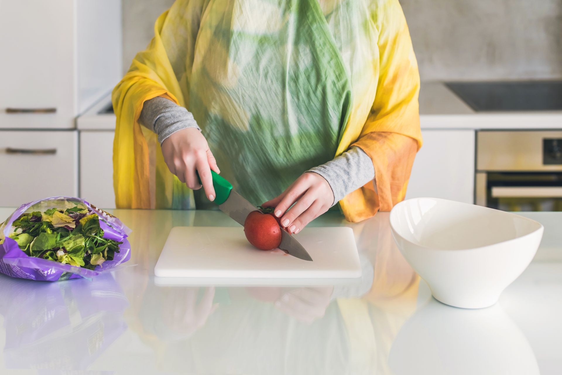 A cropped view of a woman chopping tomatoes on a kitchen benchtop to prepare a salad.