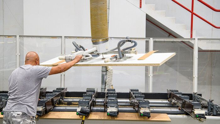 A man is lifting a piece of wood from a machine in a factory.
