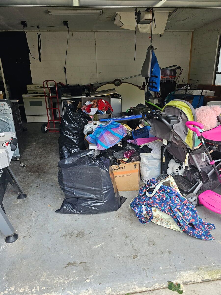 Garage filled with clutter: black trash bags, stroller, clothes, and other items.