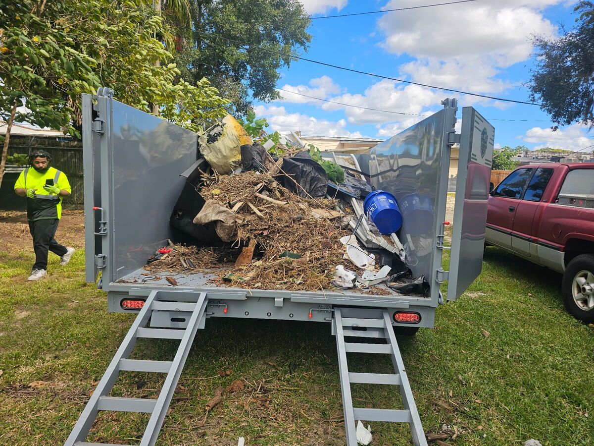 A trailer filled with debris and trash; a person in a vest walks beside the trailer.