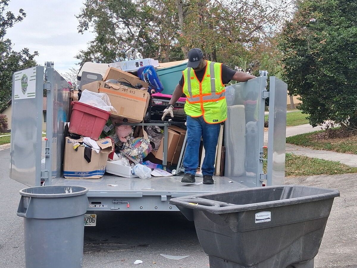 Worker in reflective vest unloading trash from truck in residential area.