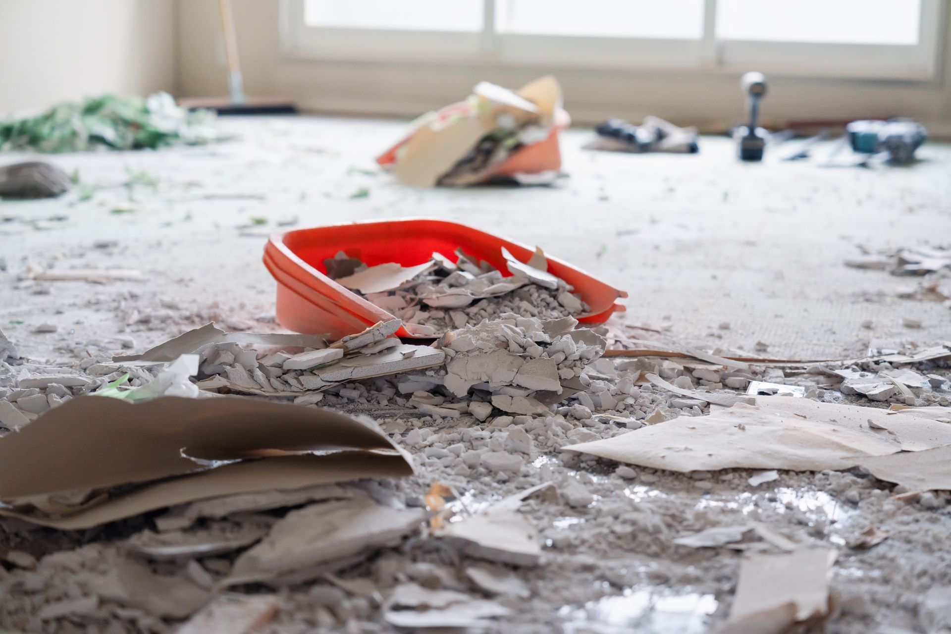 Debris on floor with a red dustpan; window in background. Construction or demolition site.