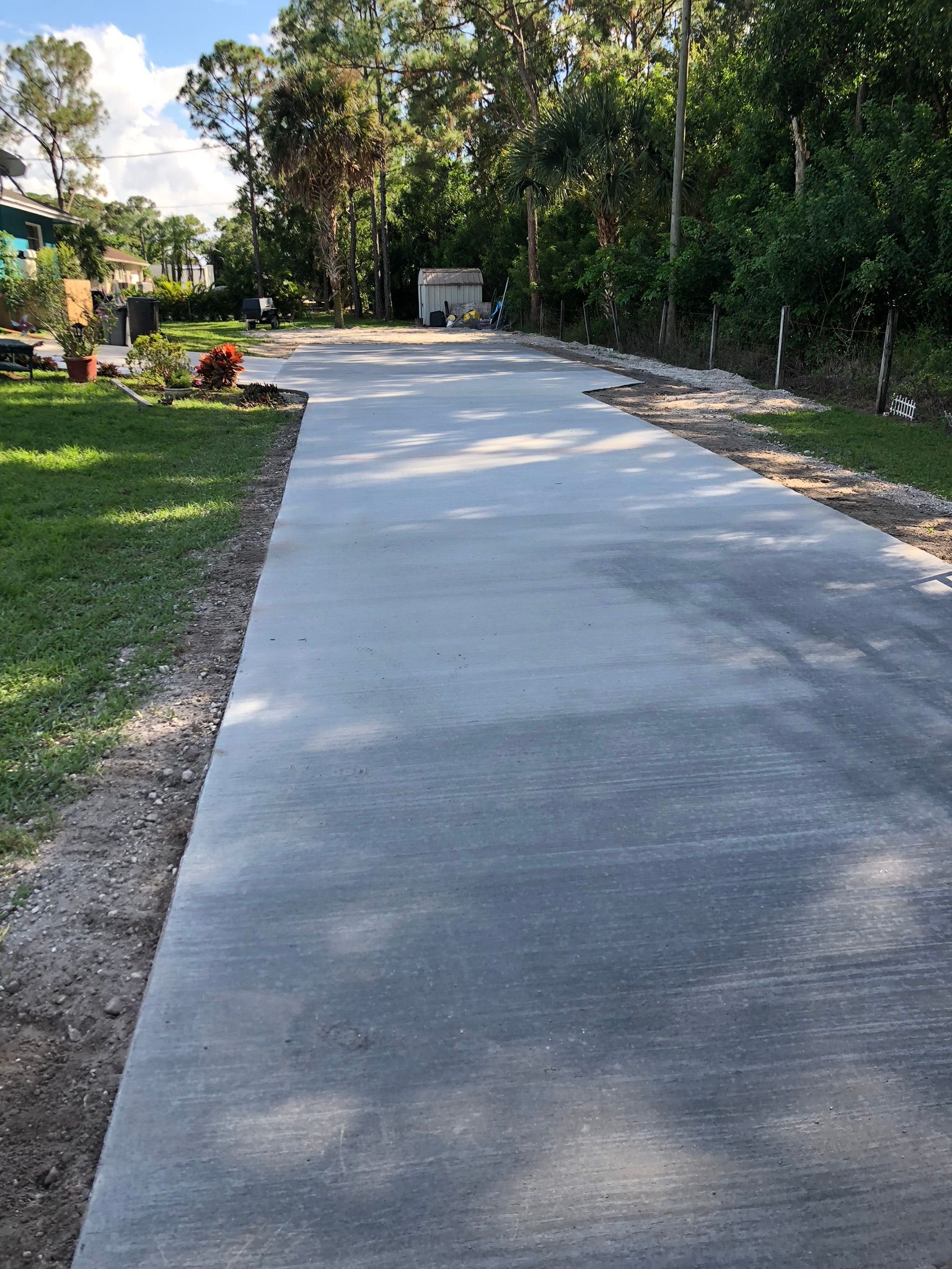 A concrete driveway leading to a house surrounded by trees and grass.