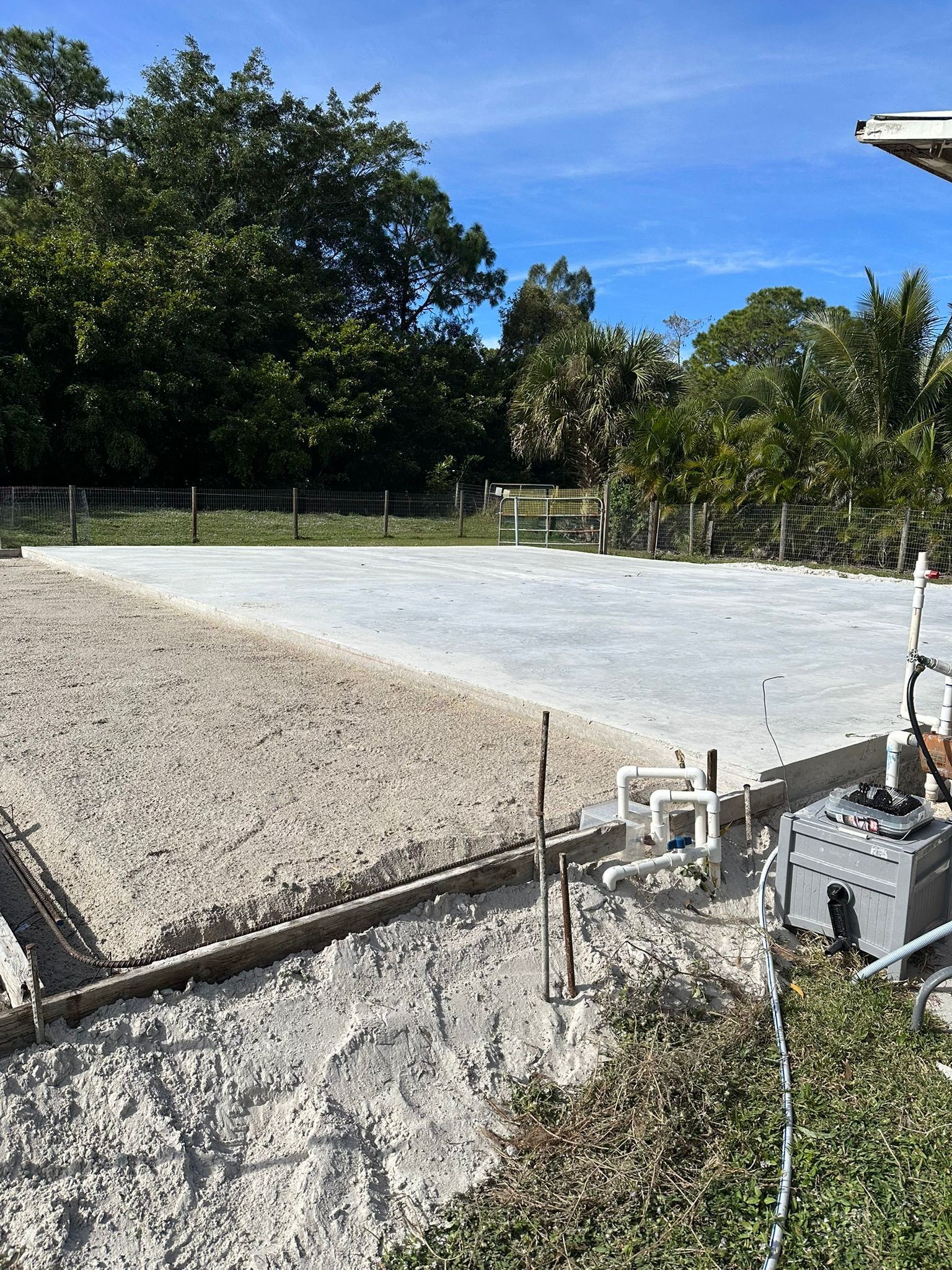 A large sandy area with a fence and trees in the background.