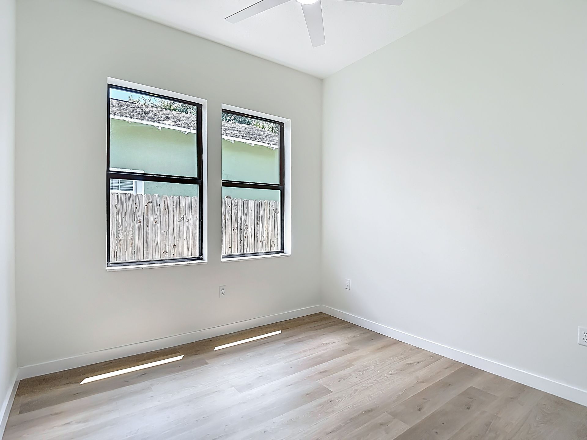Empty room with two windows, light wooden floors, and white walls.