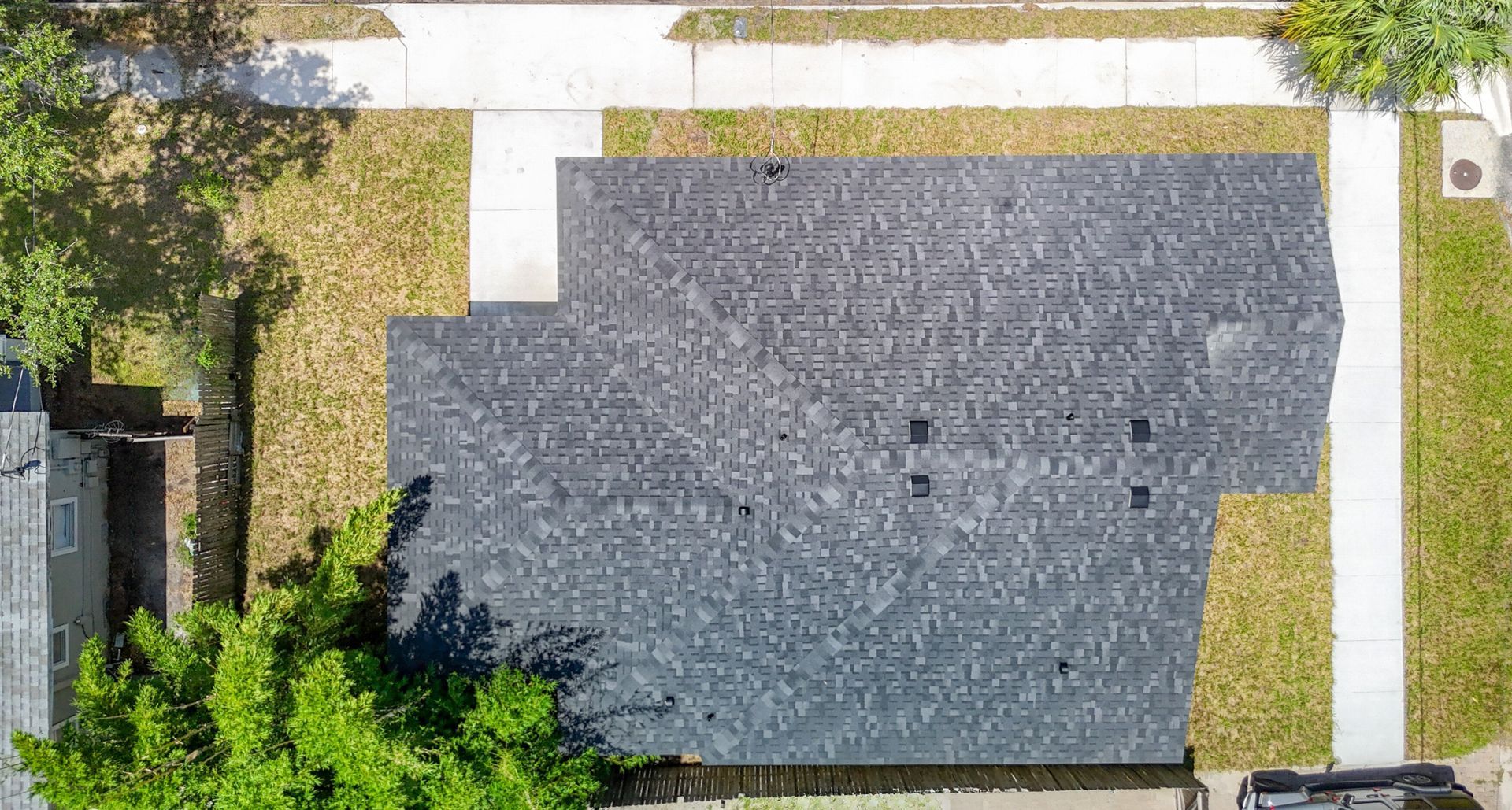 Overhead view of a house with a dark gray roof, surrounded by lawn and sidewalk.