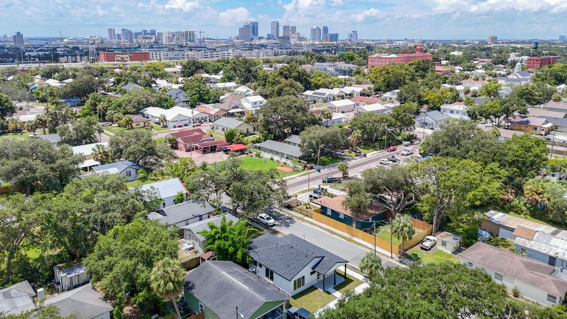Aerial view of a residential neighborhood with downtown skyline in the background, featuring houses and abundant trees.