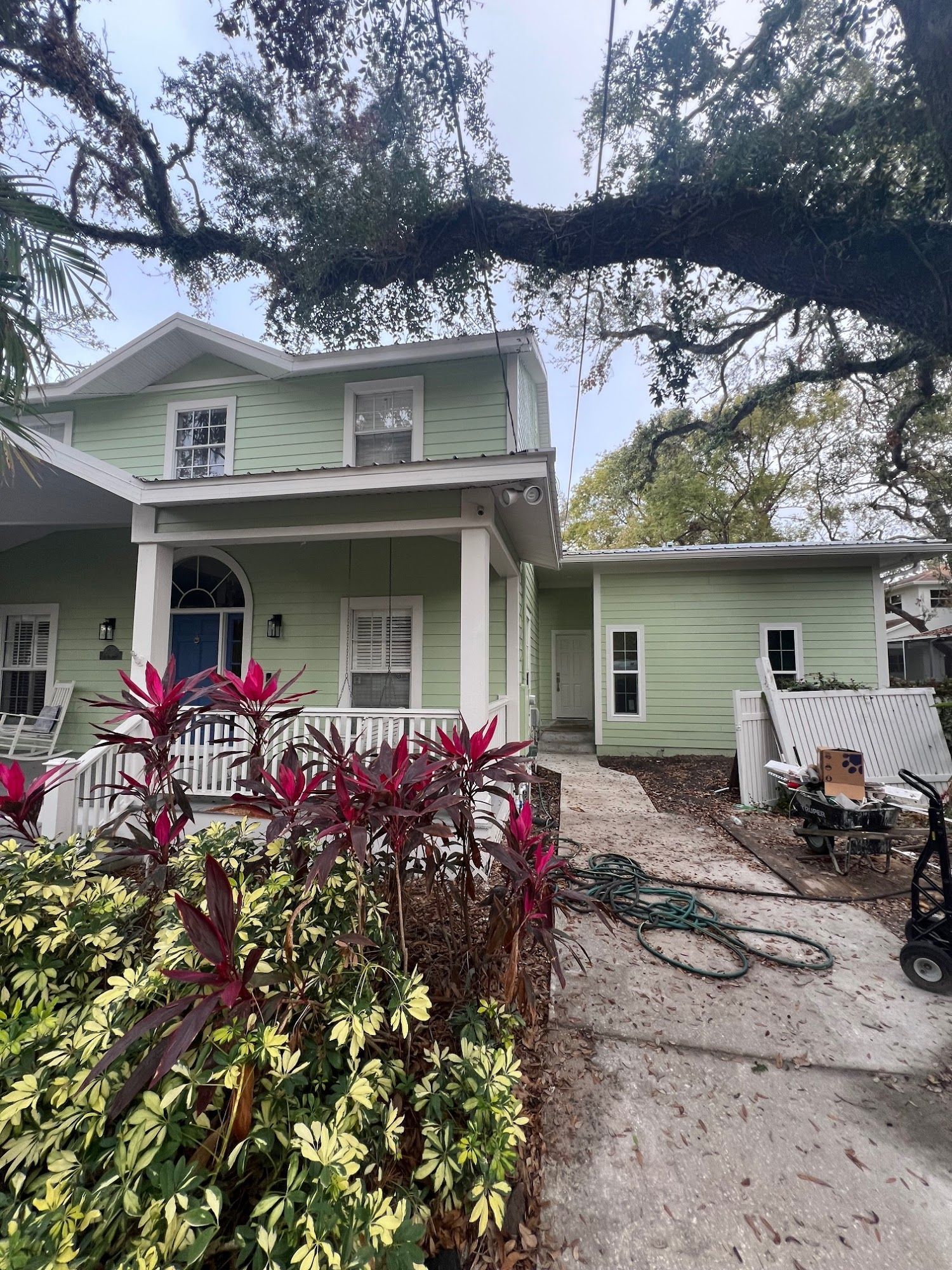 Green house with white porch and red plants in front.
