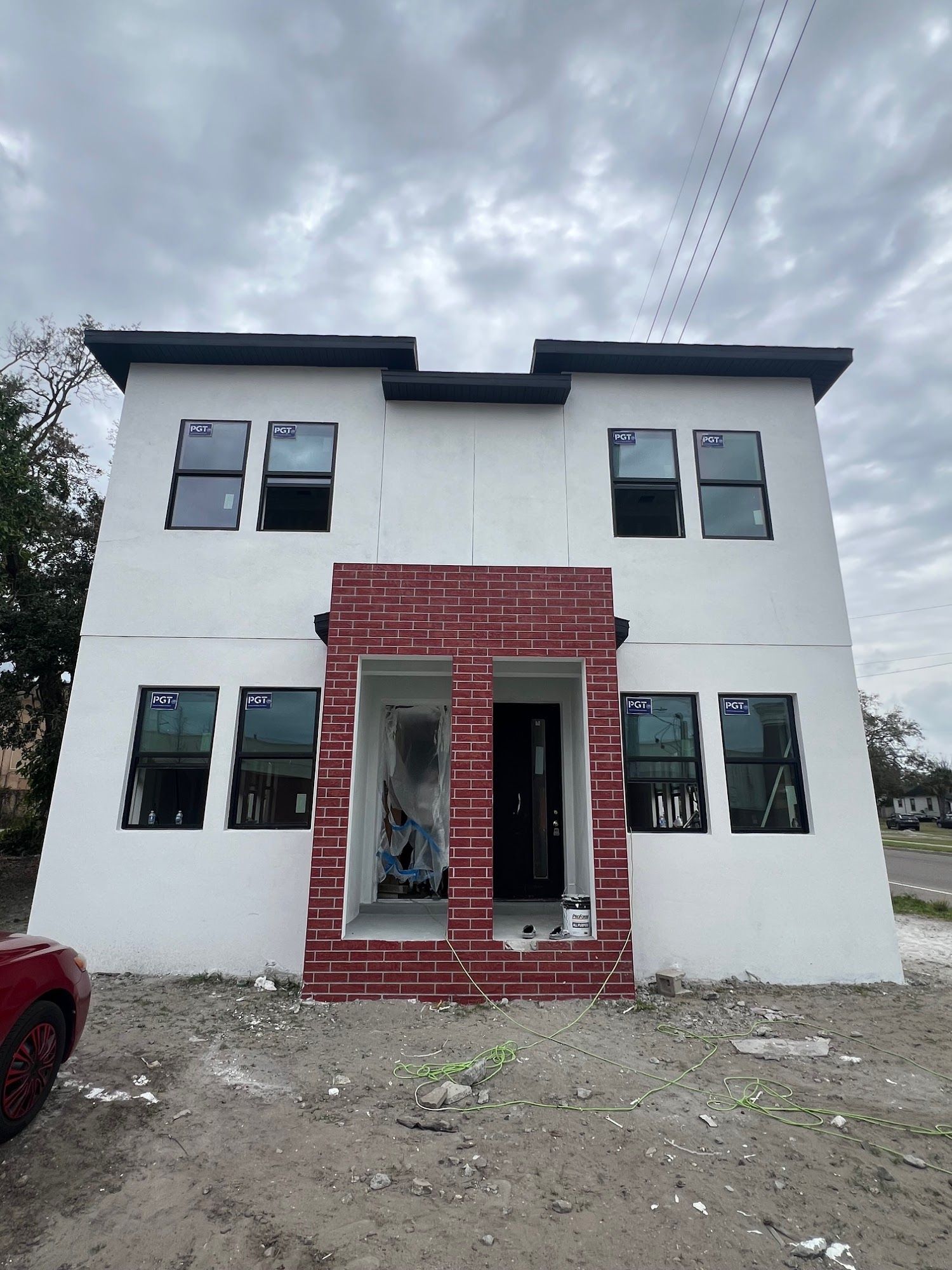 Two-story white building under construction with a brick entry and black-framed windows; cloudy sky.