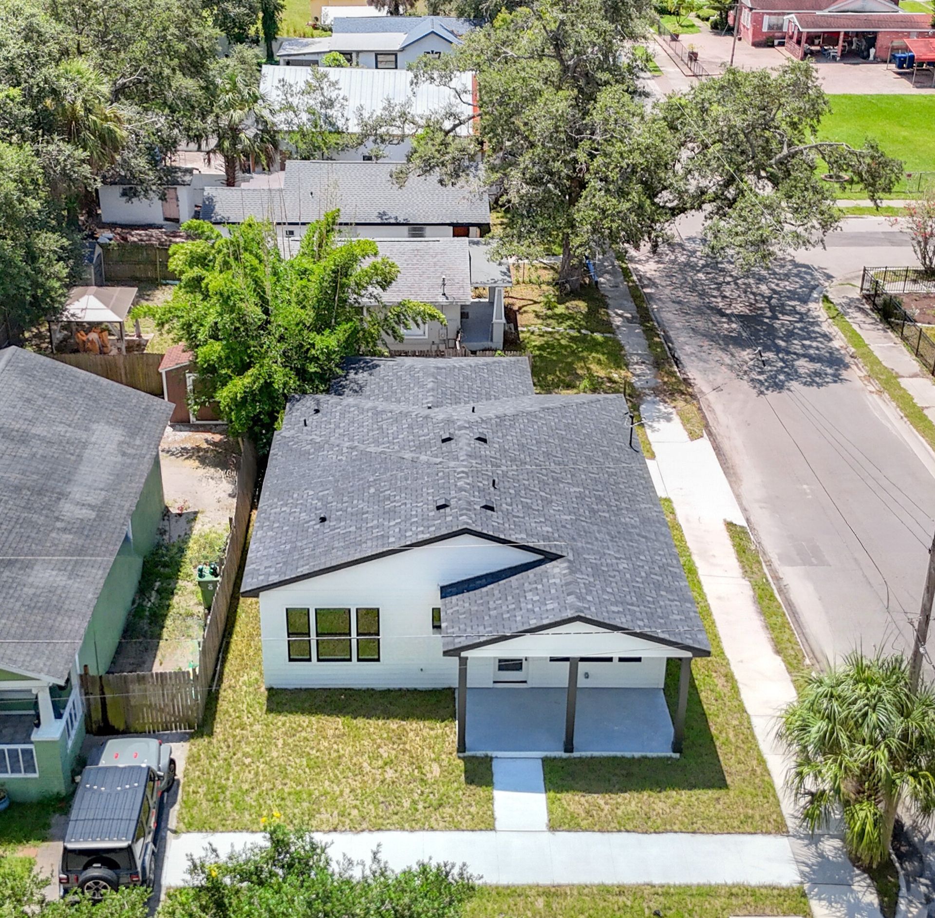 Aerial view of a white house with a dark roof and small yard on a sunny street.