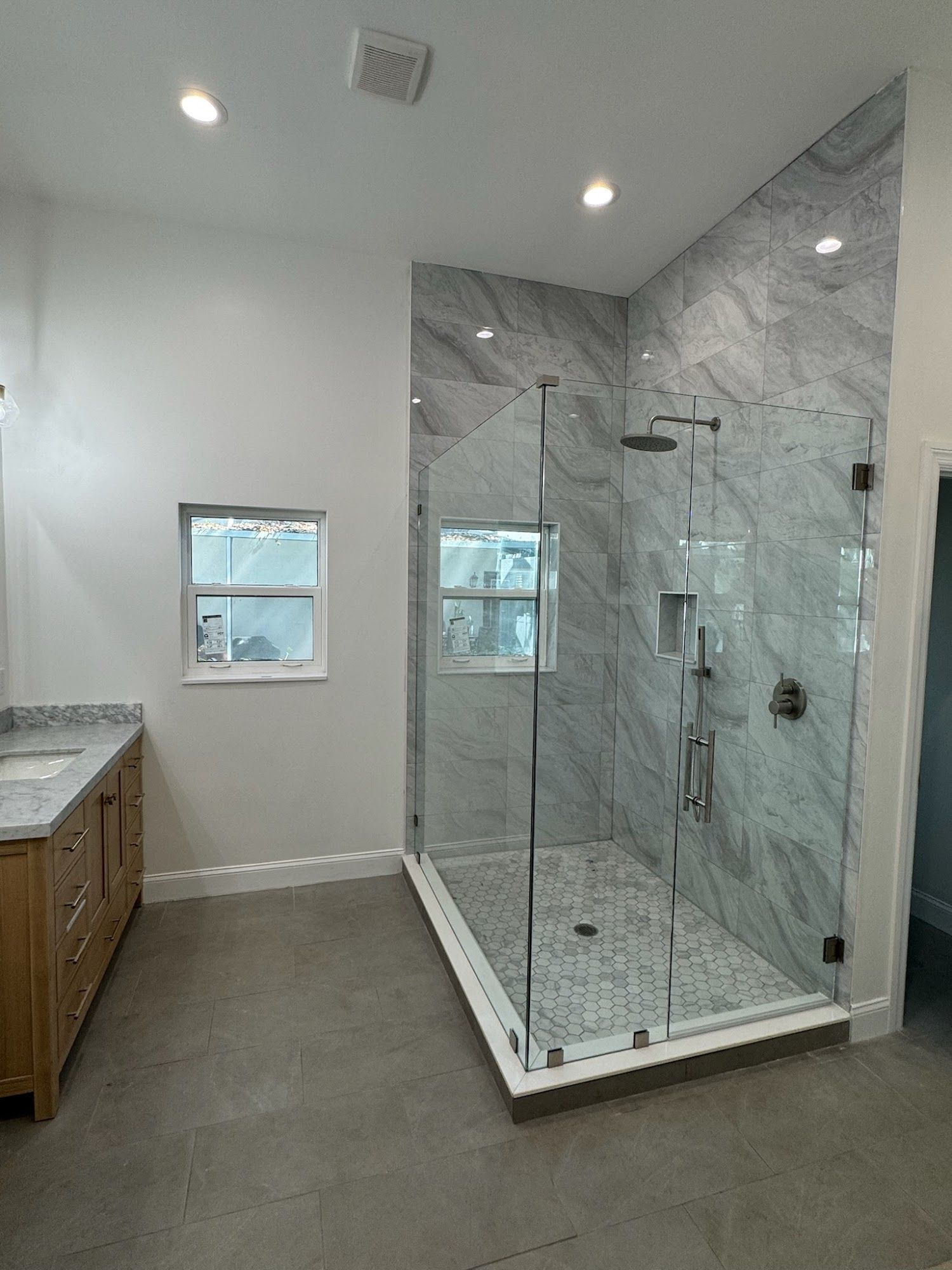 Modern bathroom with a glass shower, marble tile, and wooden vanity.