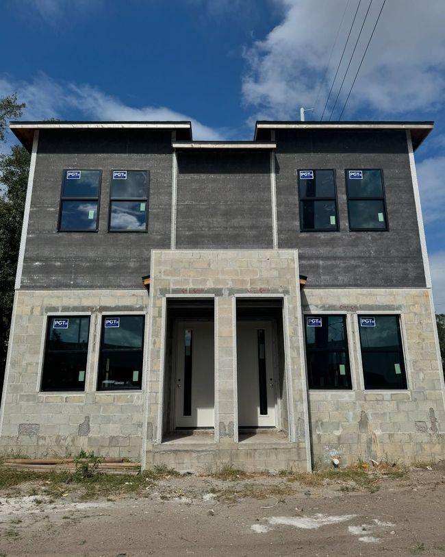 Two-story duplex under construction with cinder block base, black windows, and dark grey siding.