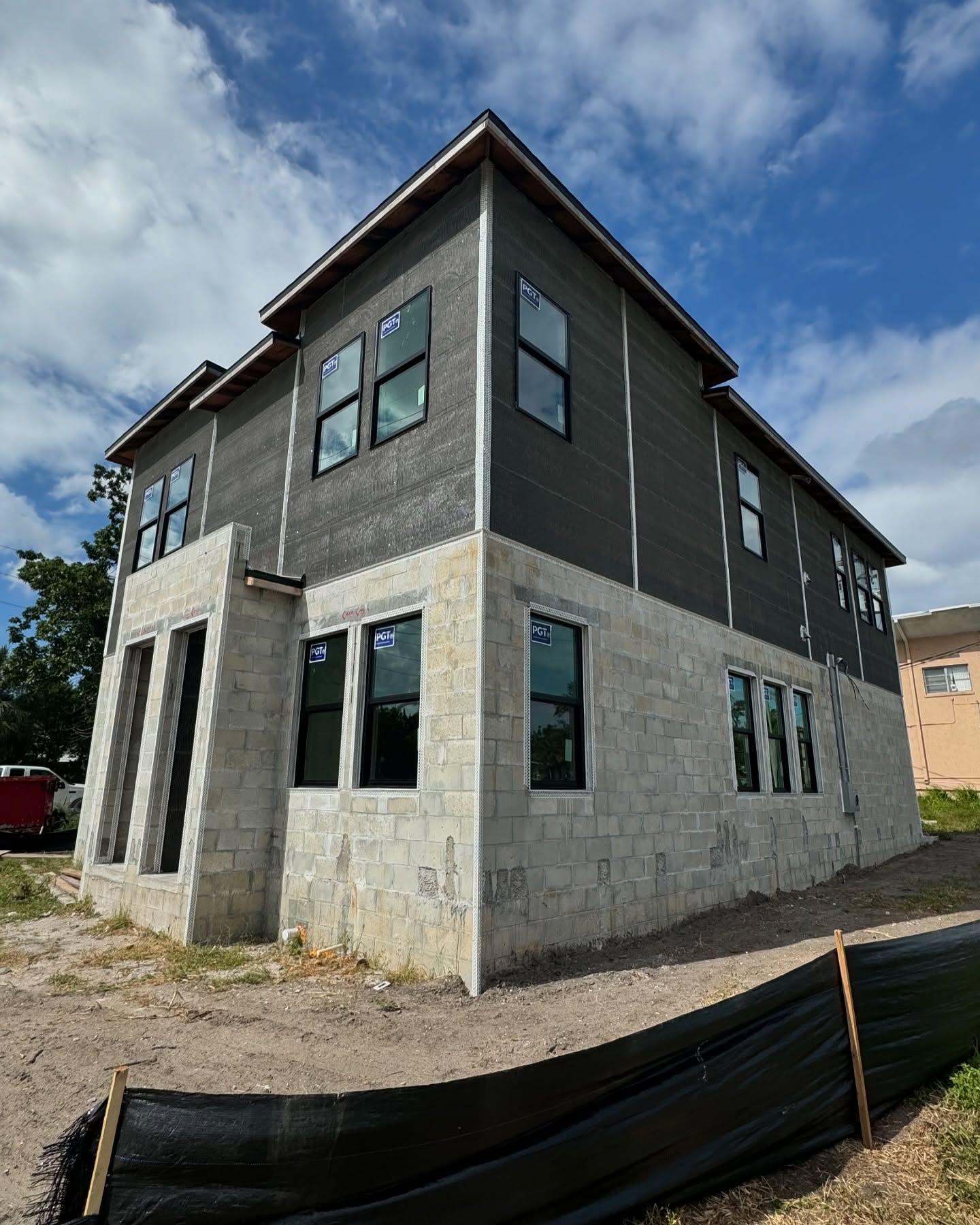 Construction of a two-story building.  Gray concrete block base, dark gray siding on upper floors, windows, blue sky.