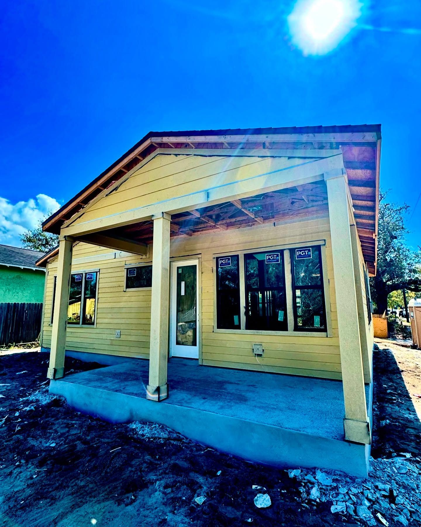 Yellow house under construction with porch and windows; bright blue sky.