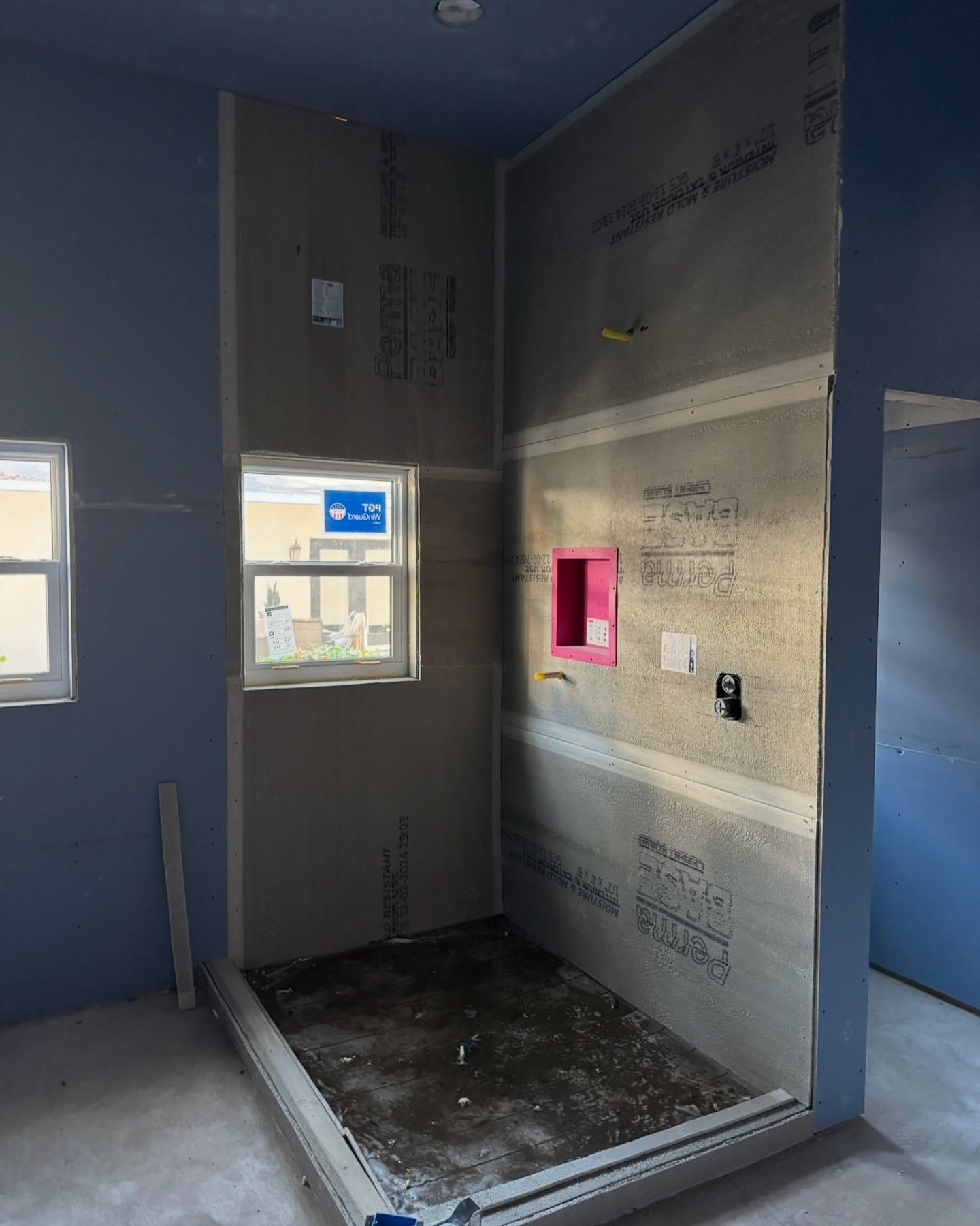 Construction of a shower in a room with blue walls, window, and gray cement board.
