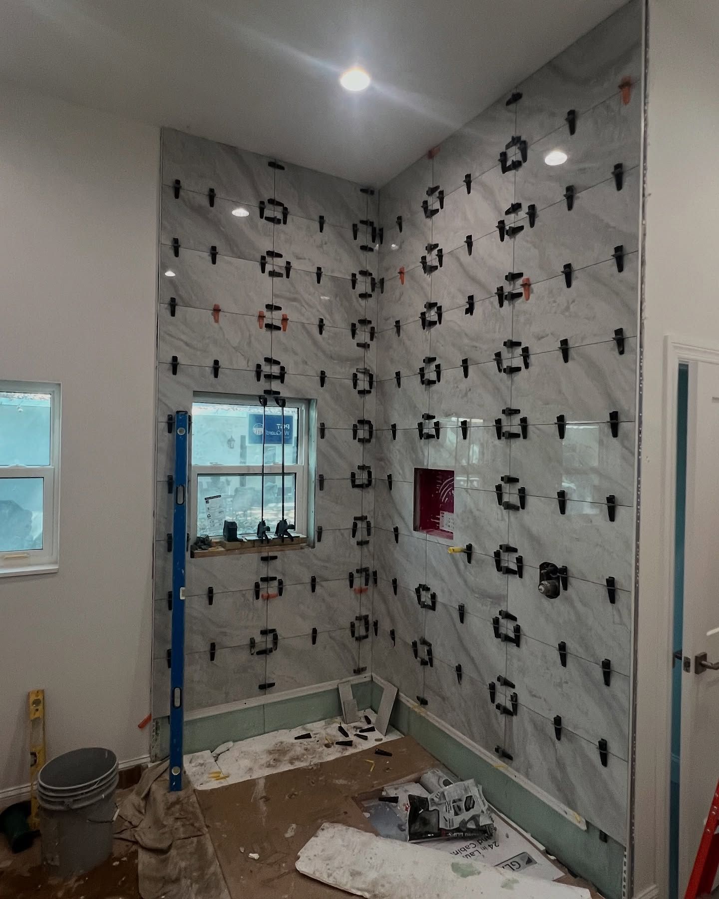 Bathroom shower walls under construction with gray and white tiles, level, spacers.