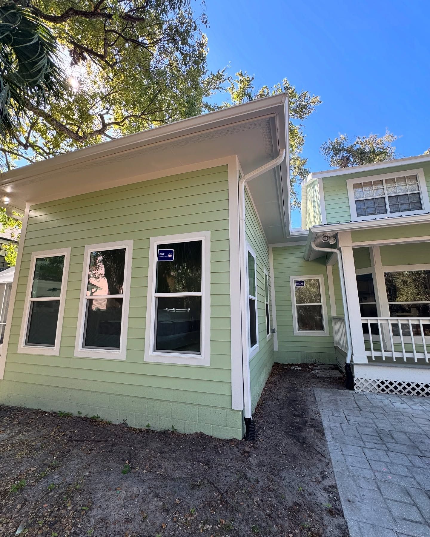 Green house with white trim, windows, and angled roof, in a sunny outdoor setting.