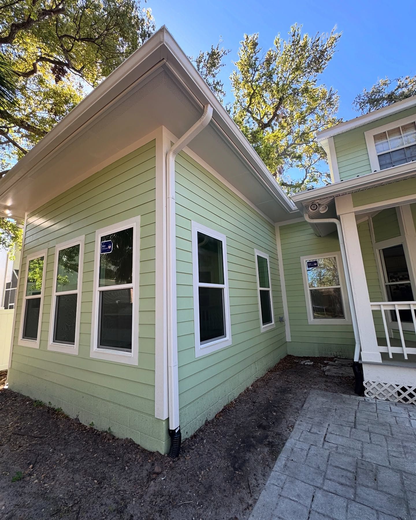 Green house with white trim, windows, and rain gutters, on a sunny day.