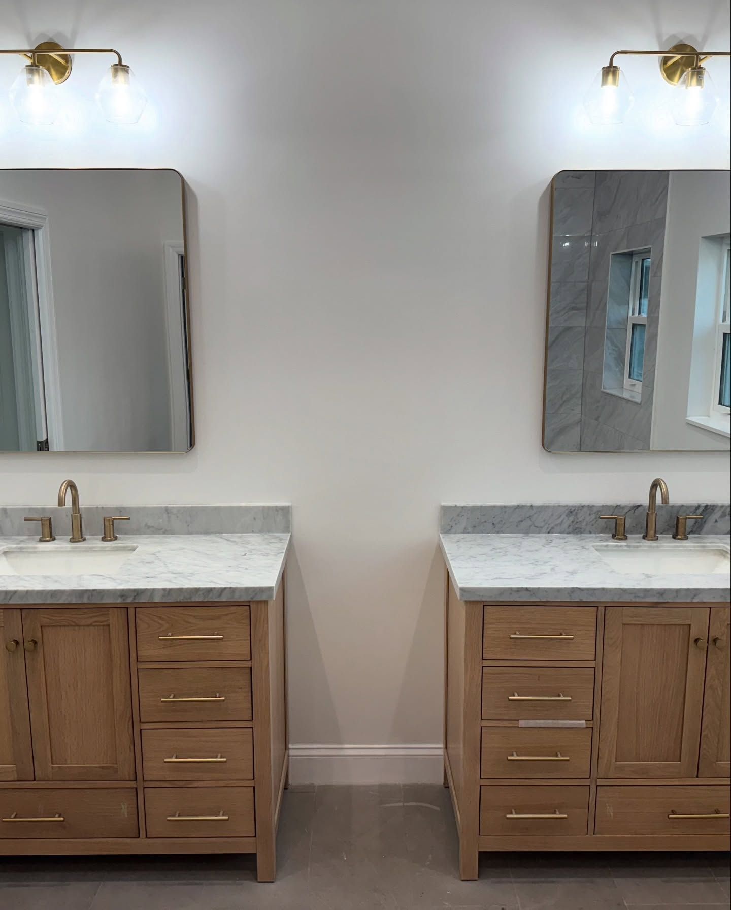 Two matching bathroom vanities with mirrors and gold fixtures.