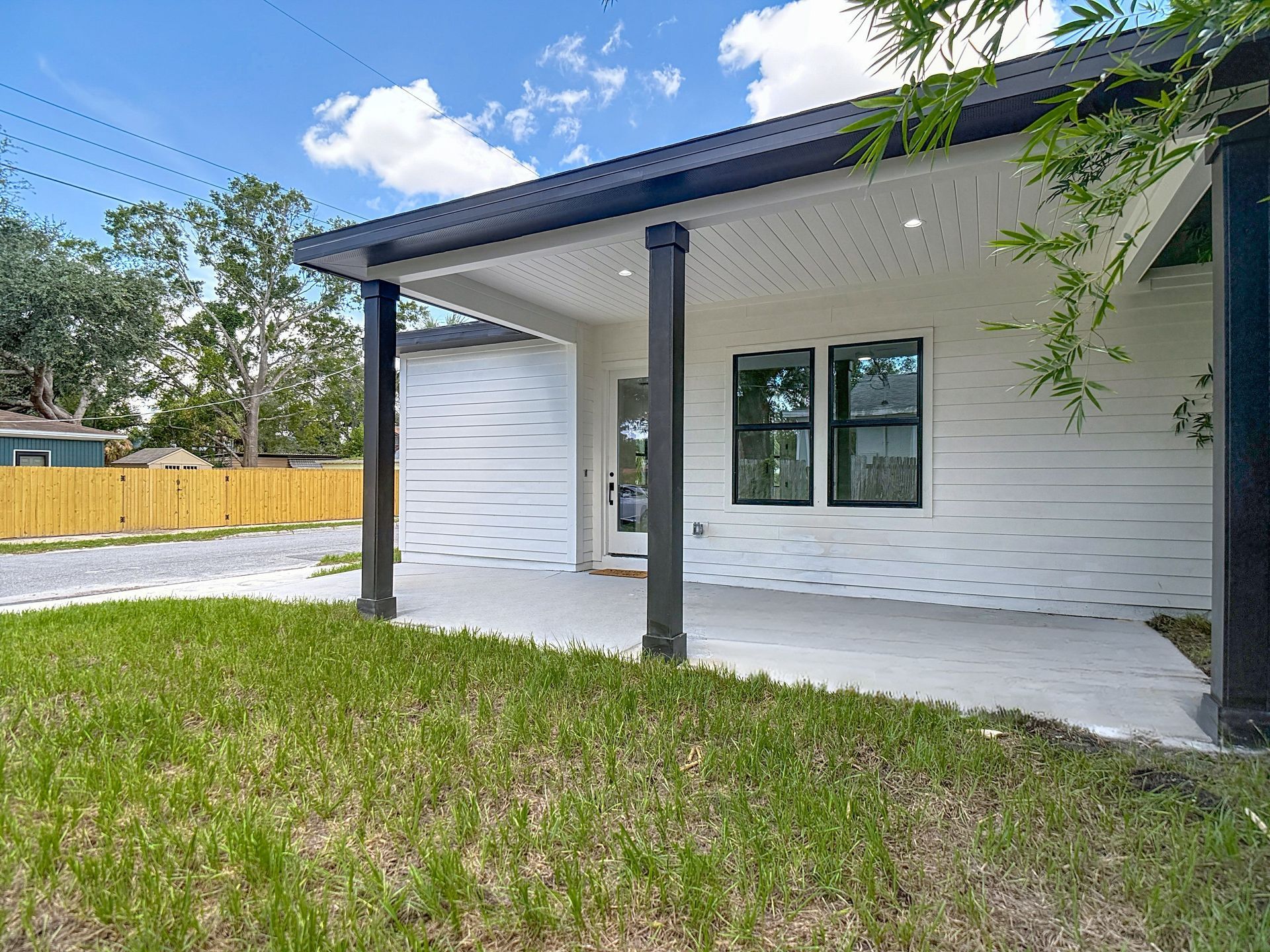 White house with covered porch, black columns, and green grass.