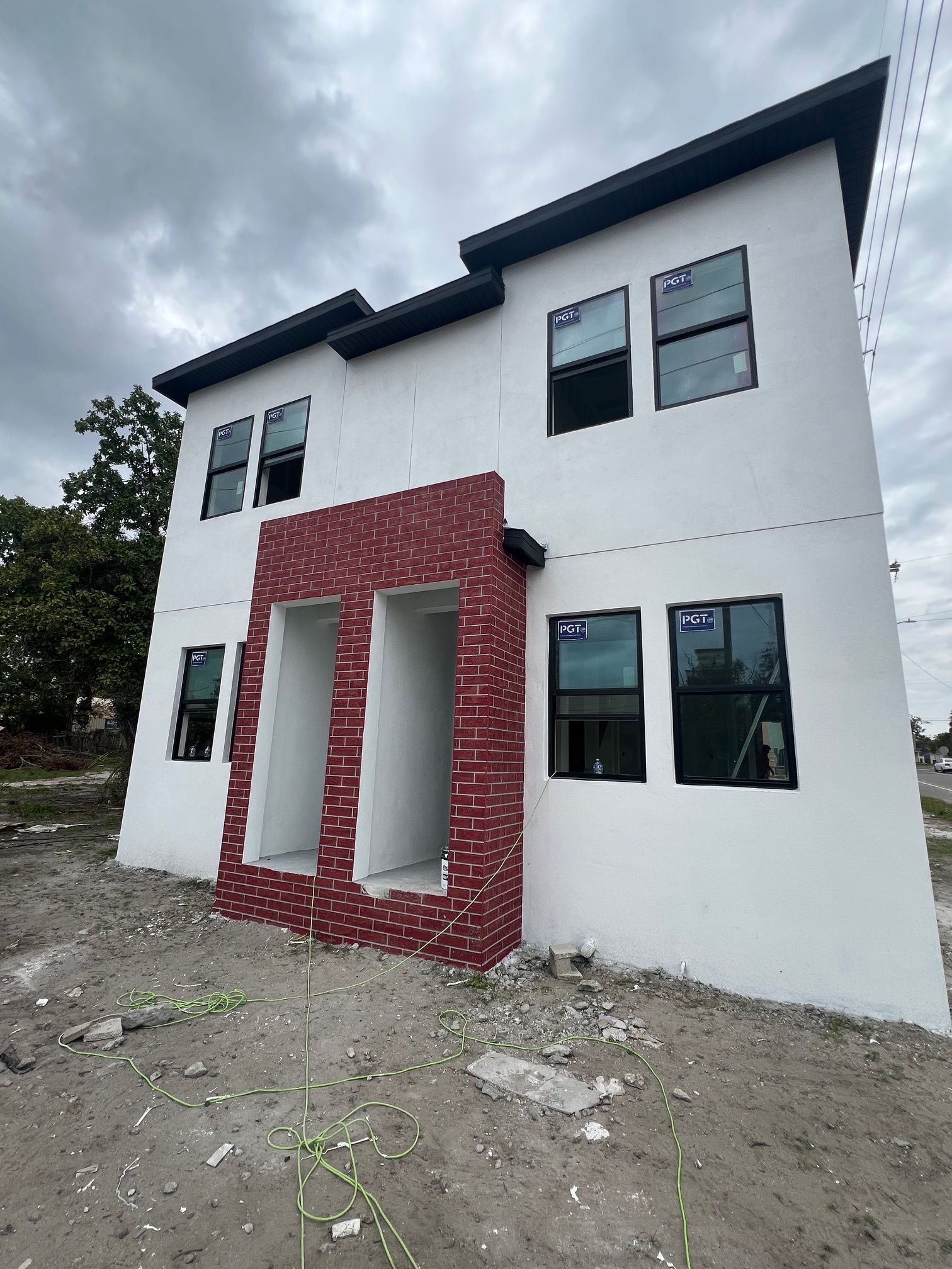 Two-story modern building under construction with white stucco and a red brick entrance under a cloudy sky.