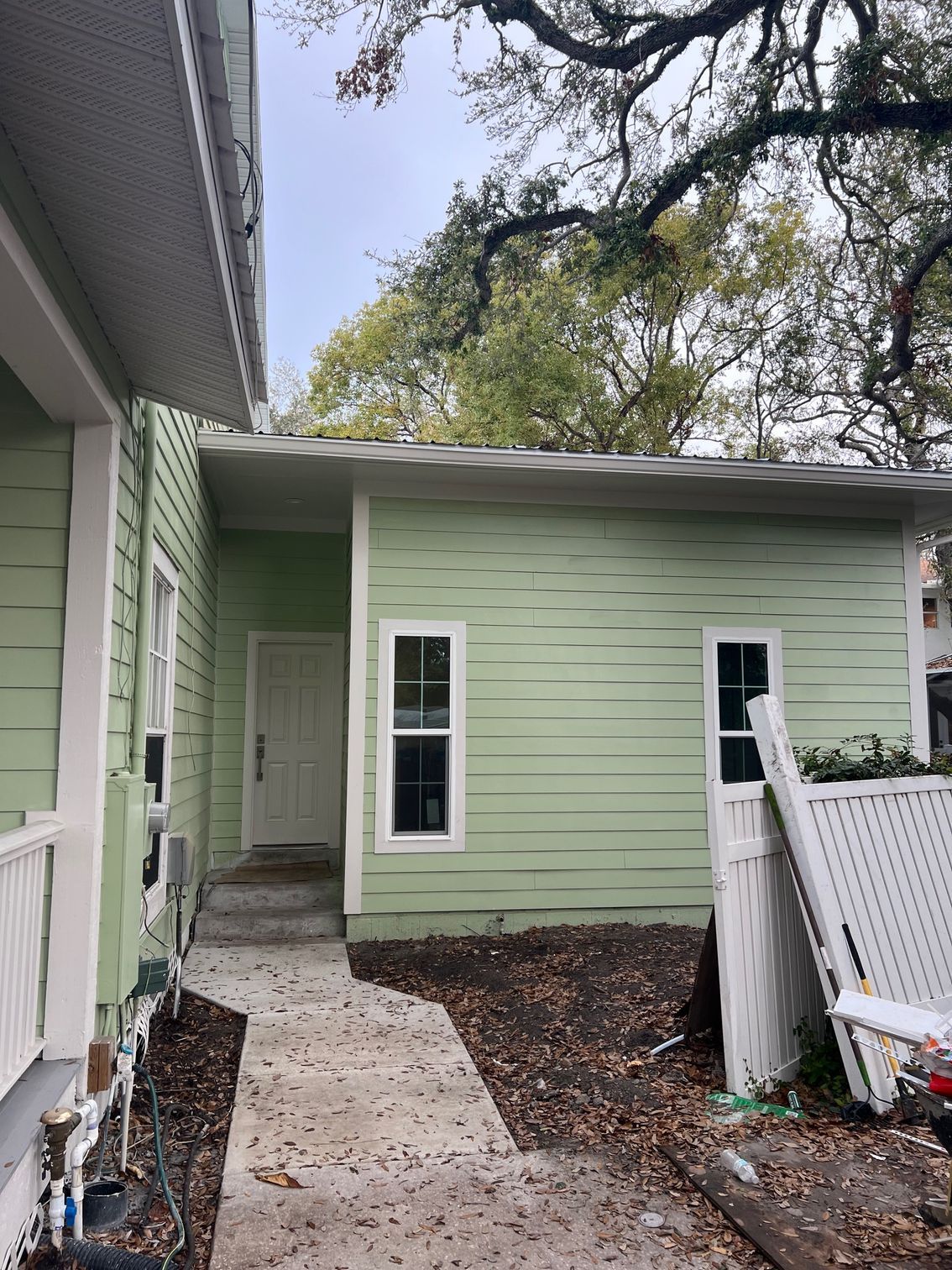 Light green building with a pathway leading to a door; a white fence is on the right.