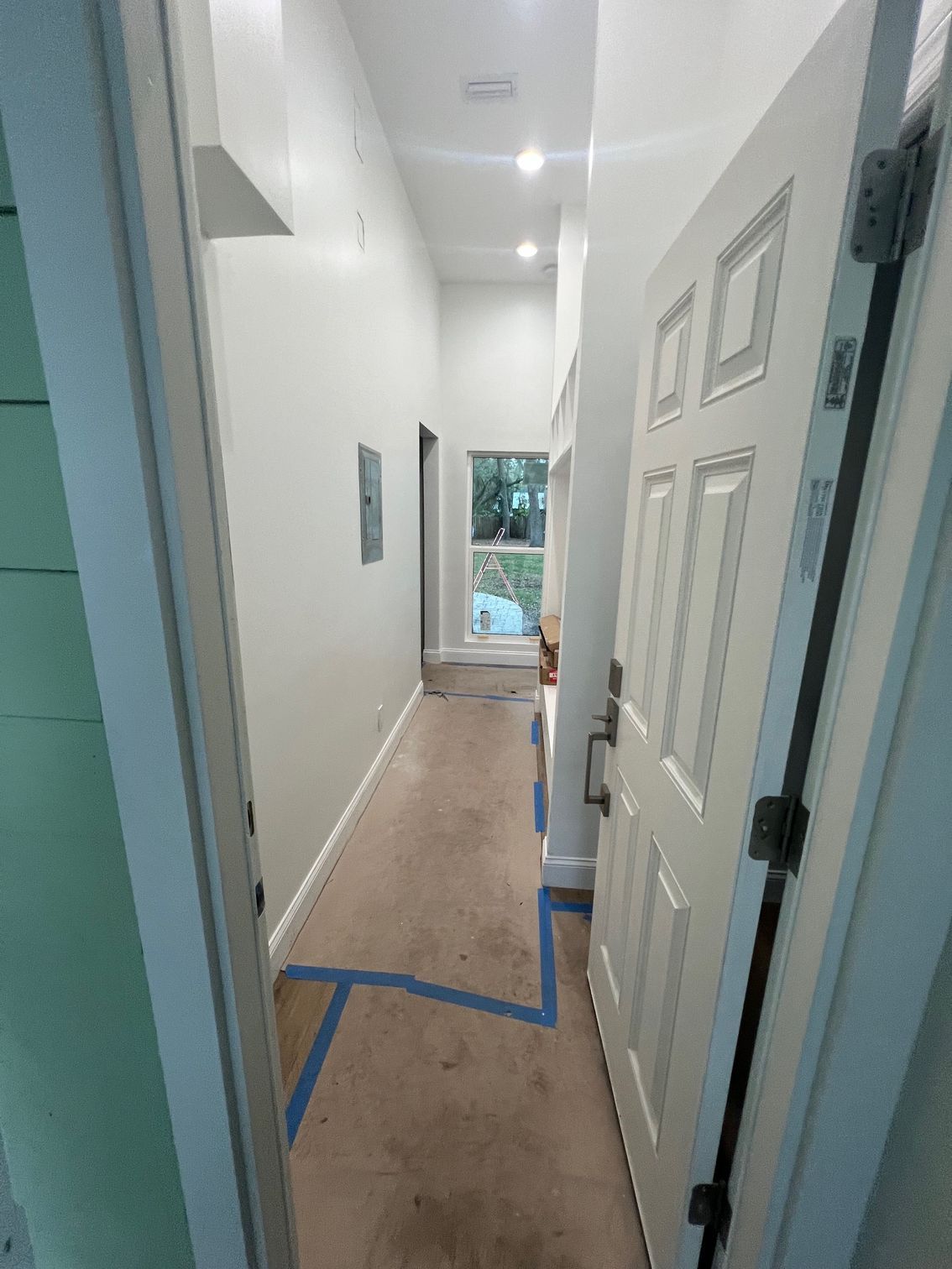 Interior hallway with a white door open to reveal a light-colored wood floor and a window at the end.