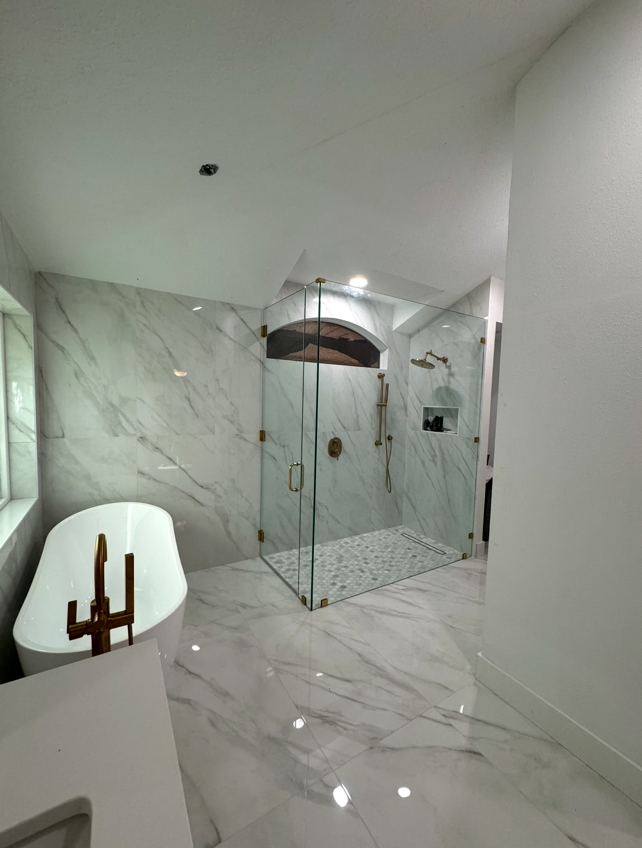 Spacious, modern bathroom with a glass shower, white marble-look tiles, and a freestanding tub.