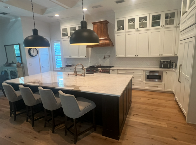 Spacious modern kitchen with white cabinets, dark island, and light wood floors. Black pendant lights over island.