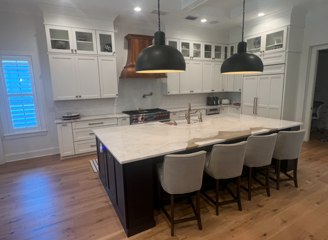 Kitchen with white cabinets, island with seating, dark pendant lights, and hardwood floors.