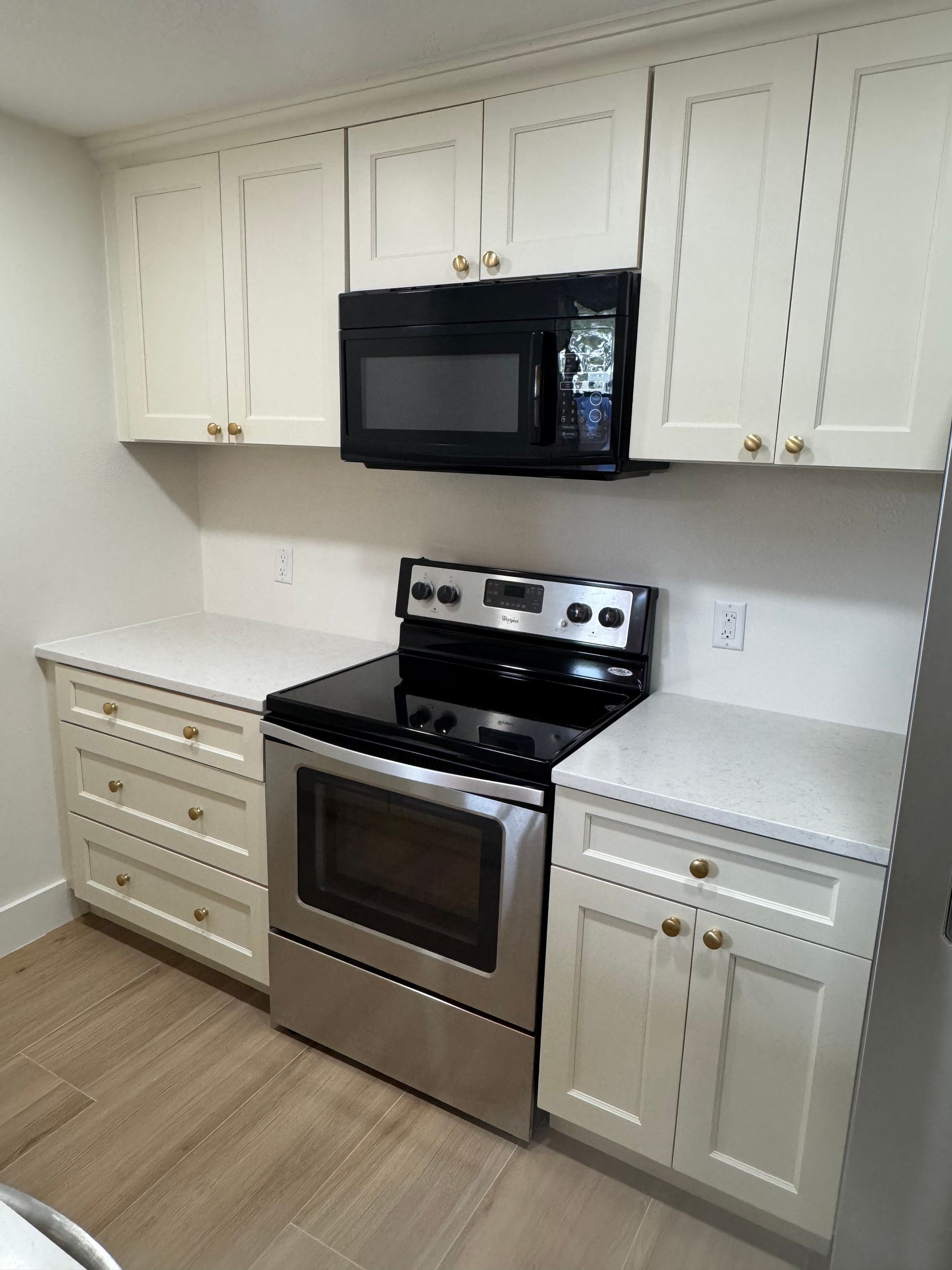 Cream-colored kitchen cabinets and counters, stainless steel oven, and black microwave.