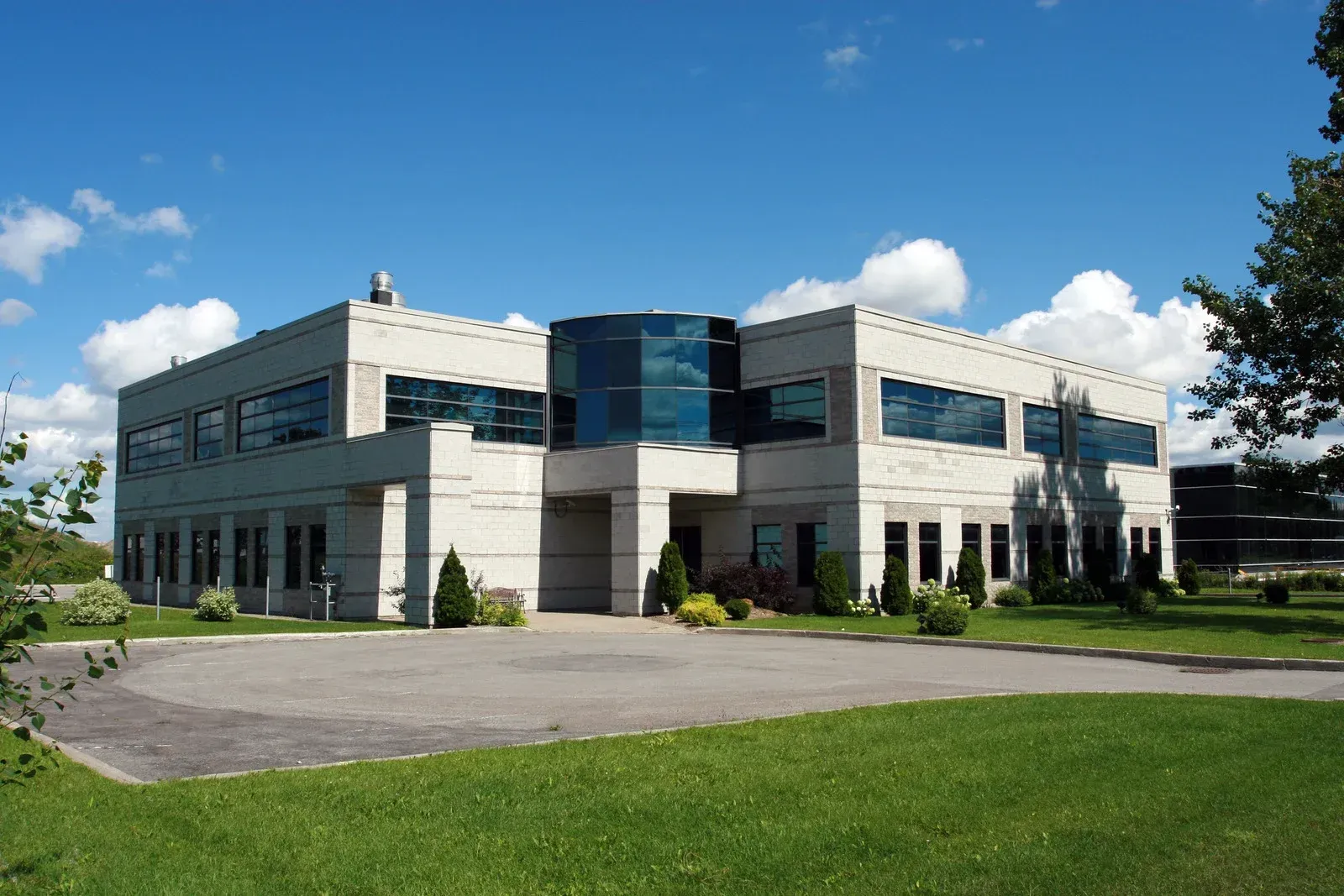 Two-story modern building with blue glass entrance, on a green lawn, under a blue sky.