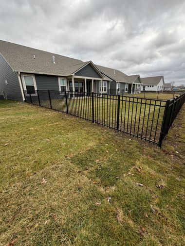 Backyard with black metal fence beside a gray house under cloudy sky