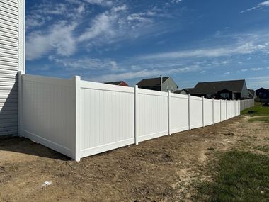 White vinyl privacy fence along a backyard, with a house on the left and cloudy blue sky above.