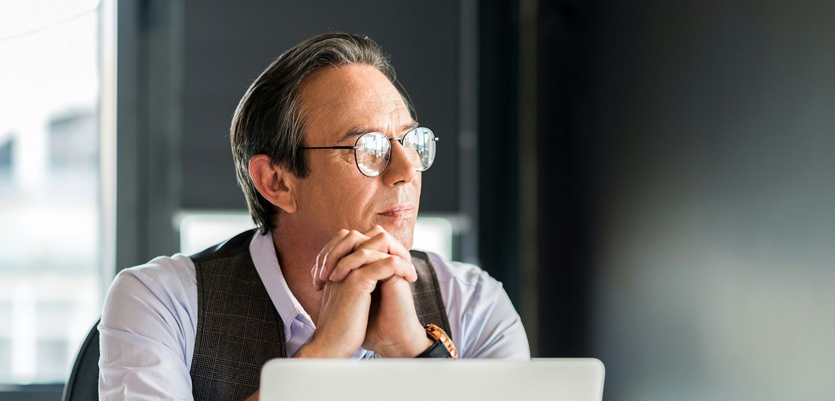 A man wearing glasses is sitting in front of a laptop computer.