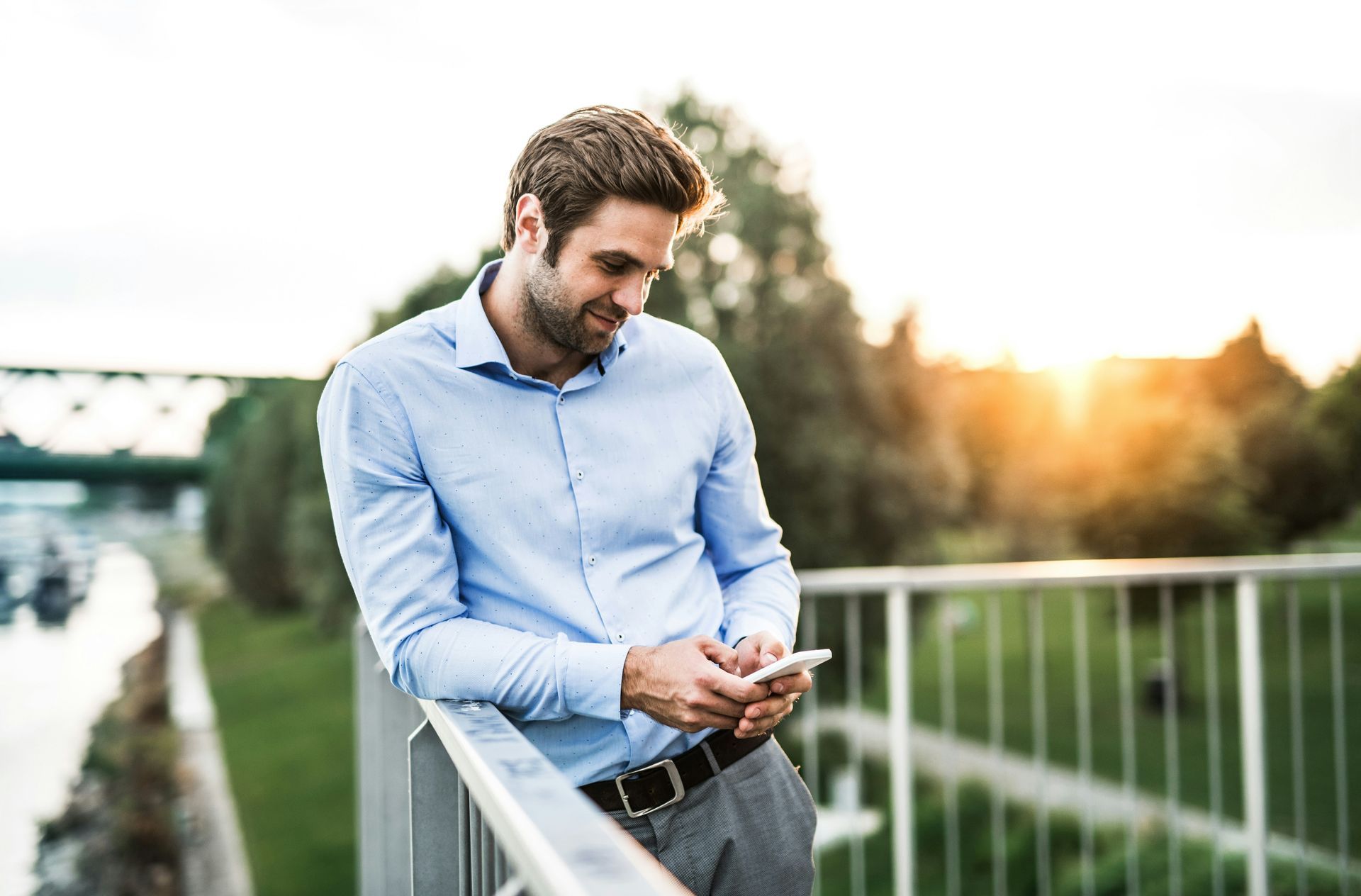 A man is leaning on a railing looking at his cell phone.