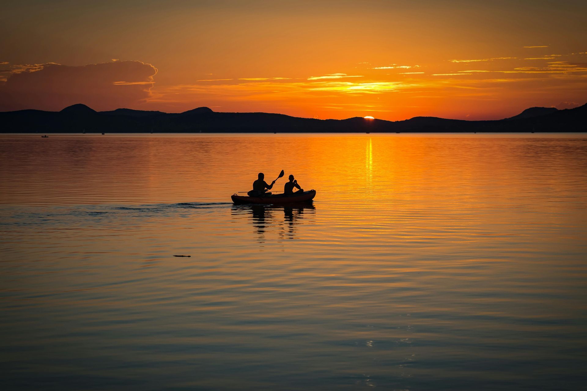 A couple of people in a boat on a lake at sunset.