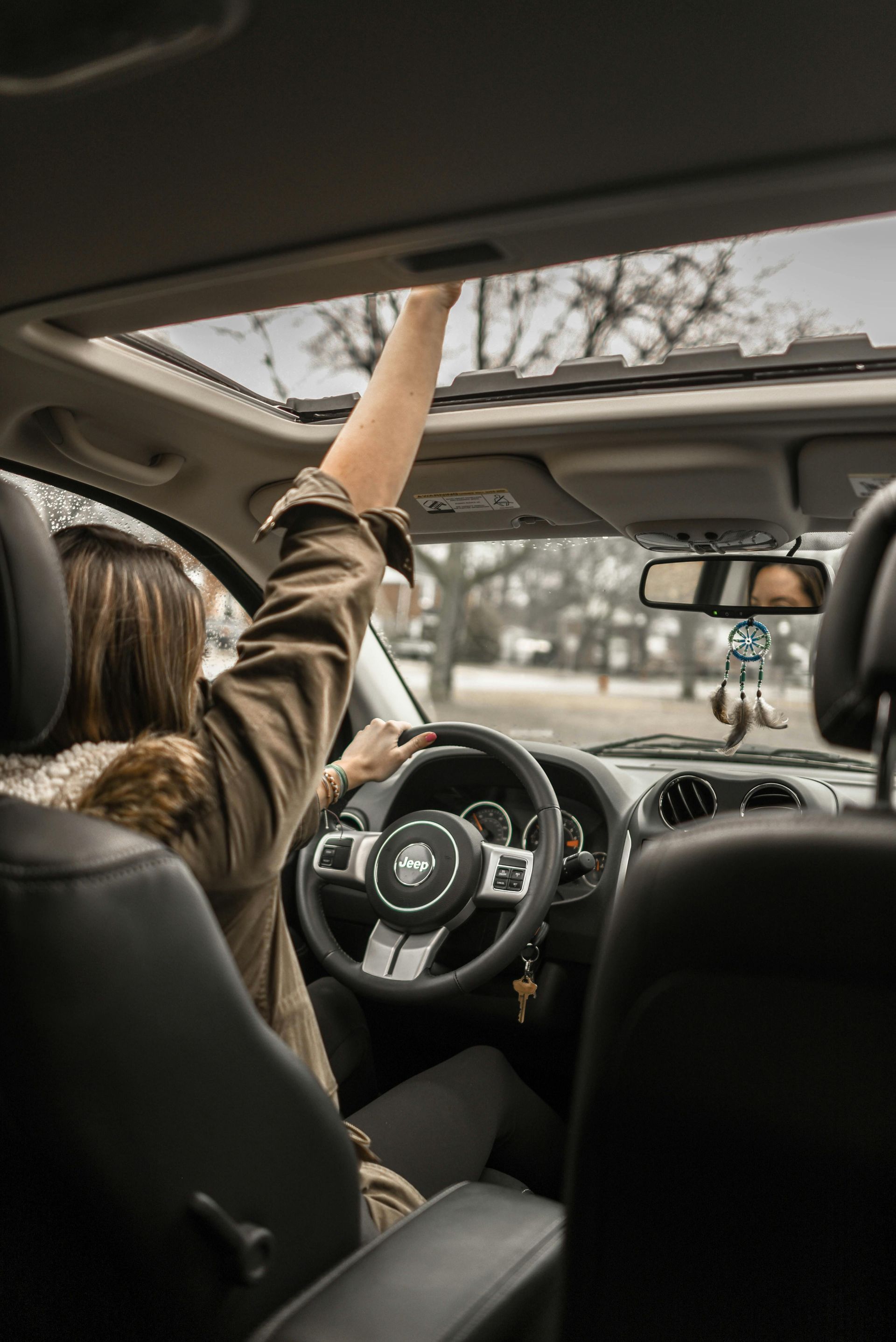 A woman is driving a car with her arms in the air.