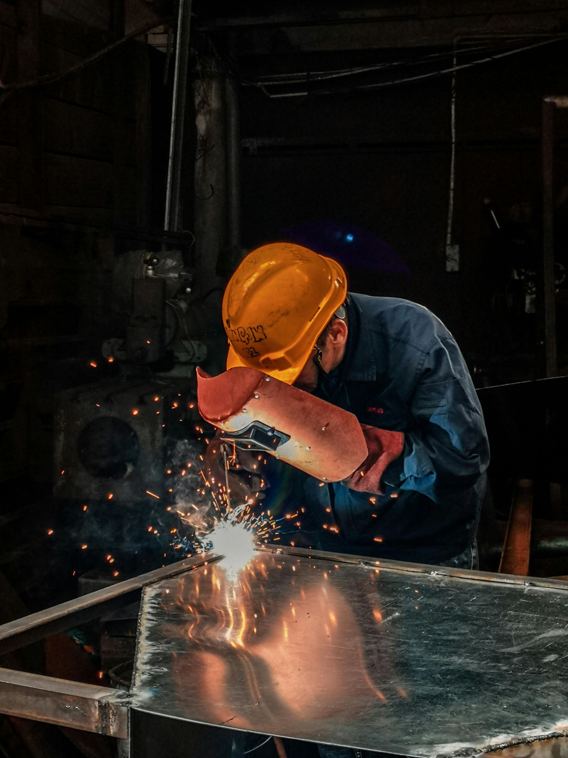 A man wearing a hard hat and gloves is welding a piece of metal.