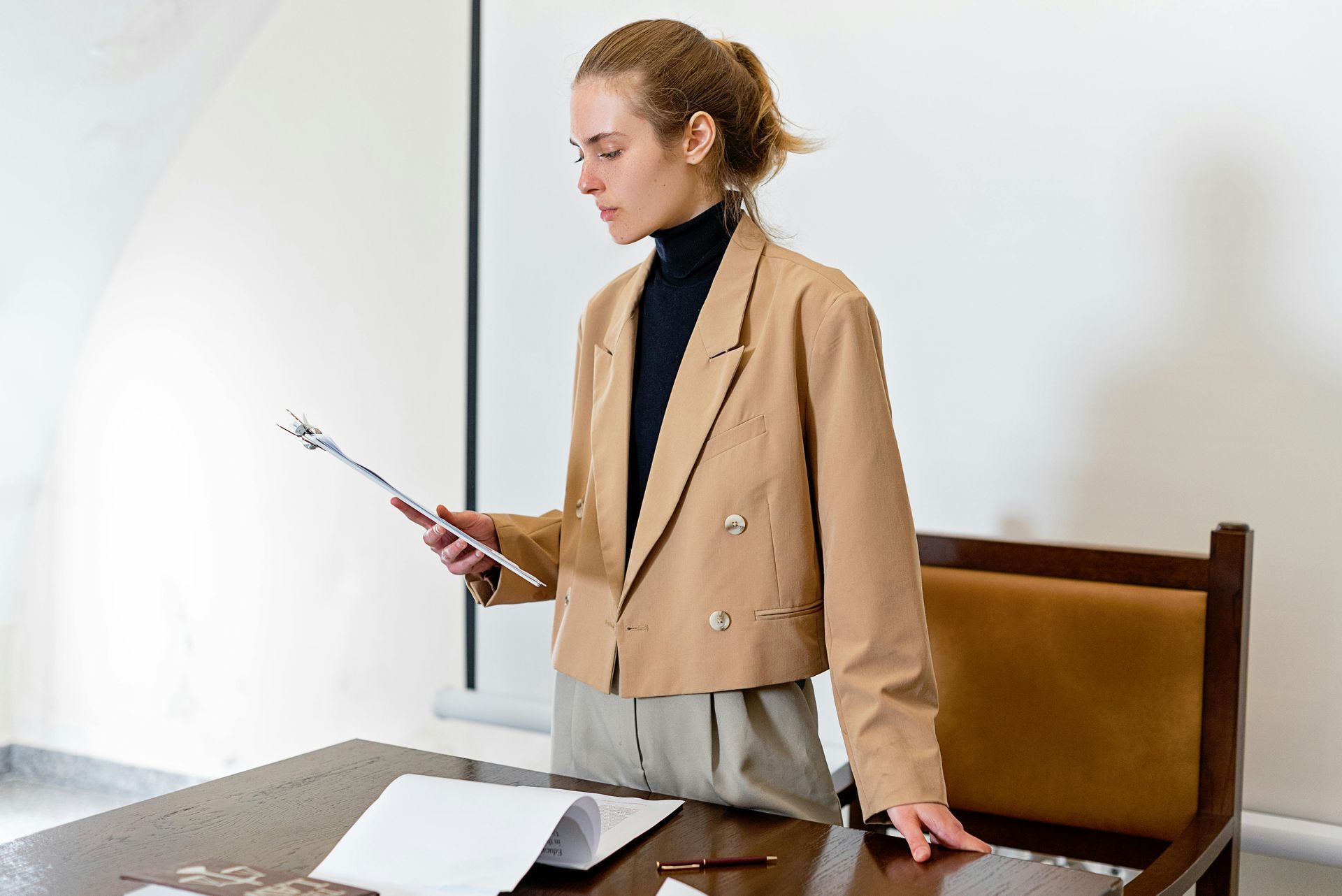 A woman is standing in front of a desk holding a clipboard.