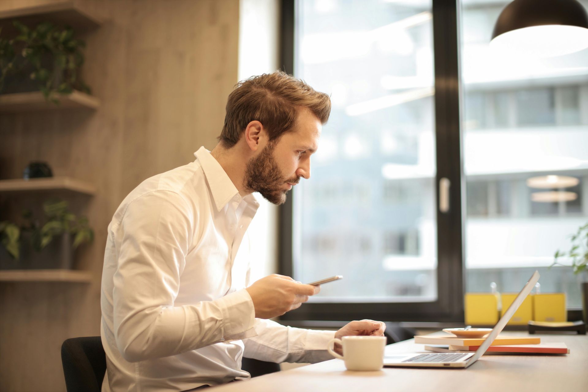 A man is sitting at a table using a laptop and a cell phone.