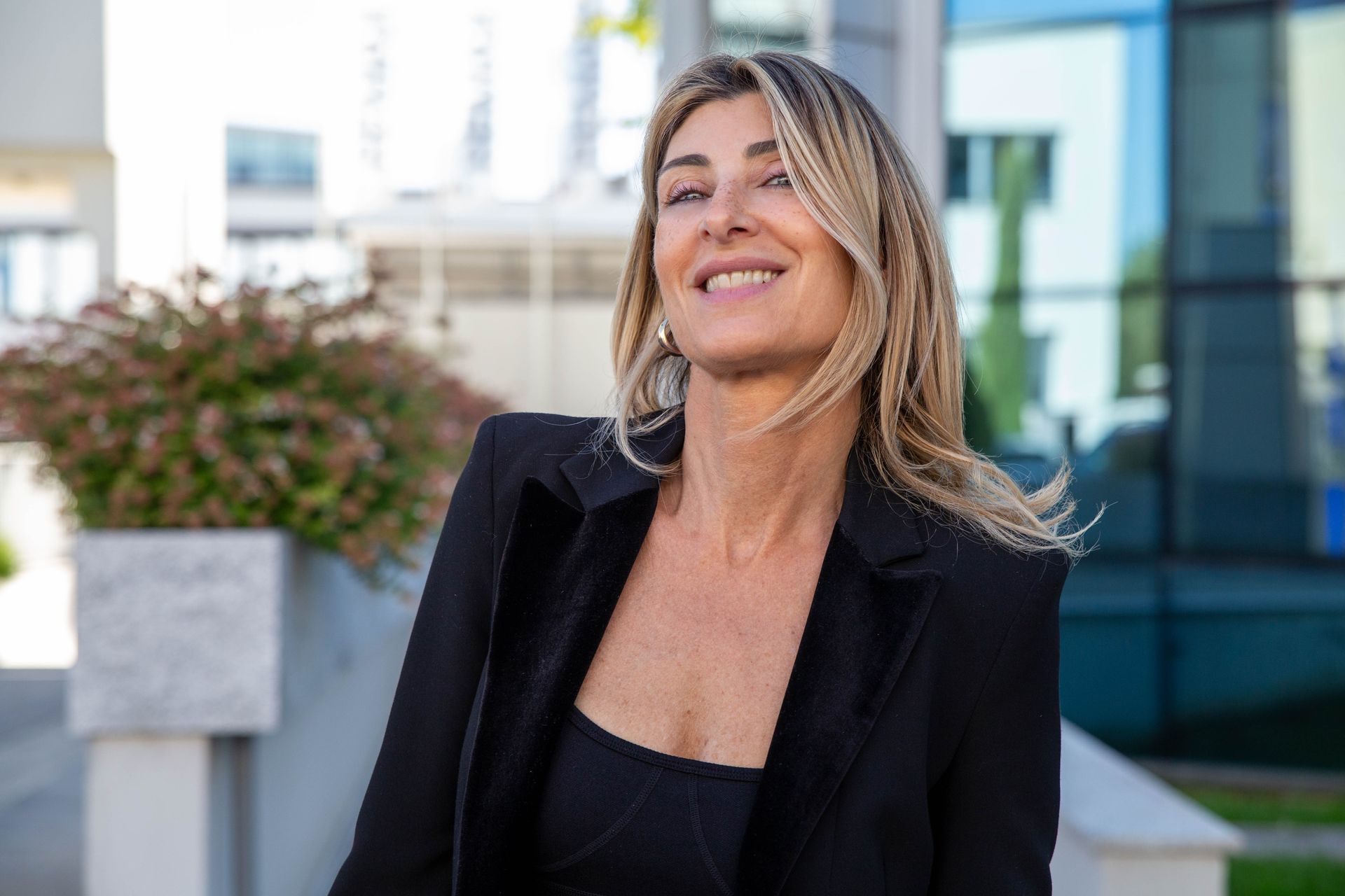 Donna con le braccia incrociate, sorridente, che indossa una giacca nera e un orologio.