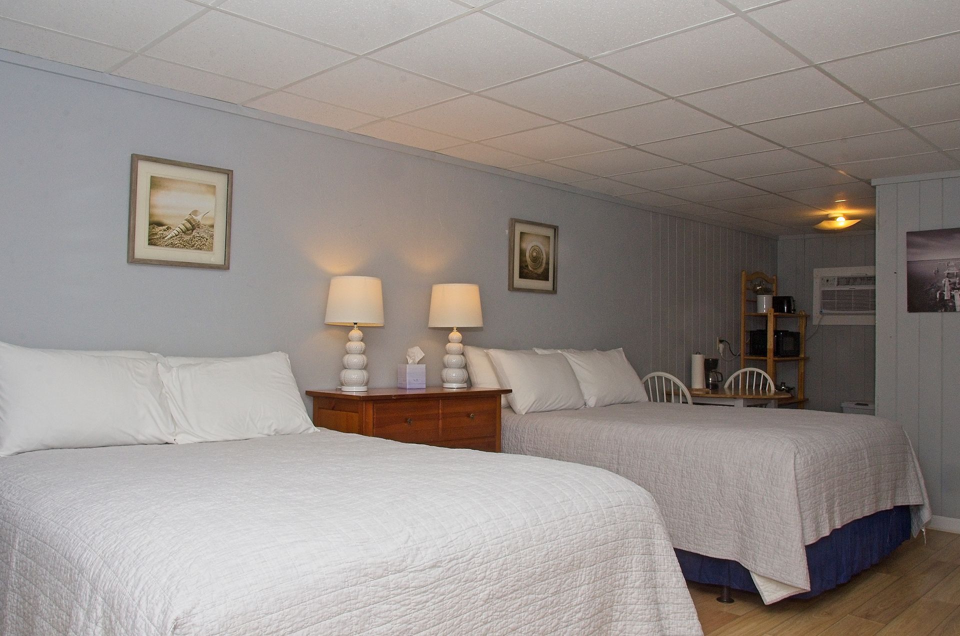 A hotel room featuring two double beds with white bedding, bedside lamps, artwork, and light blue walls.