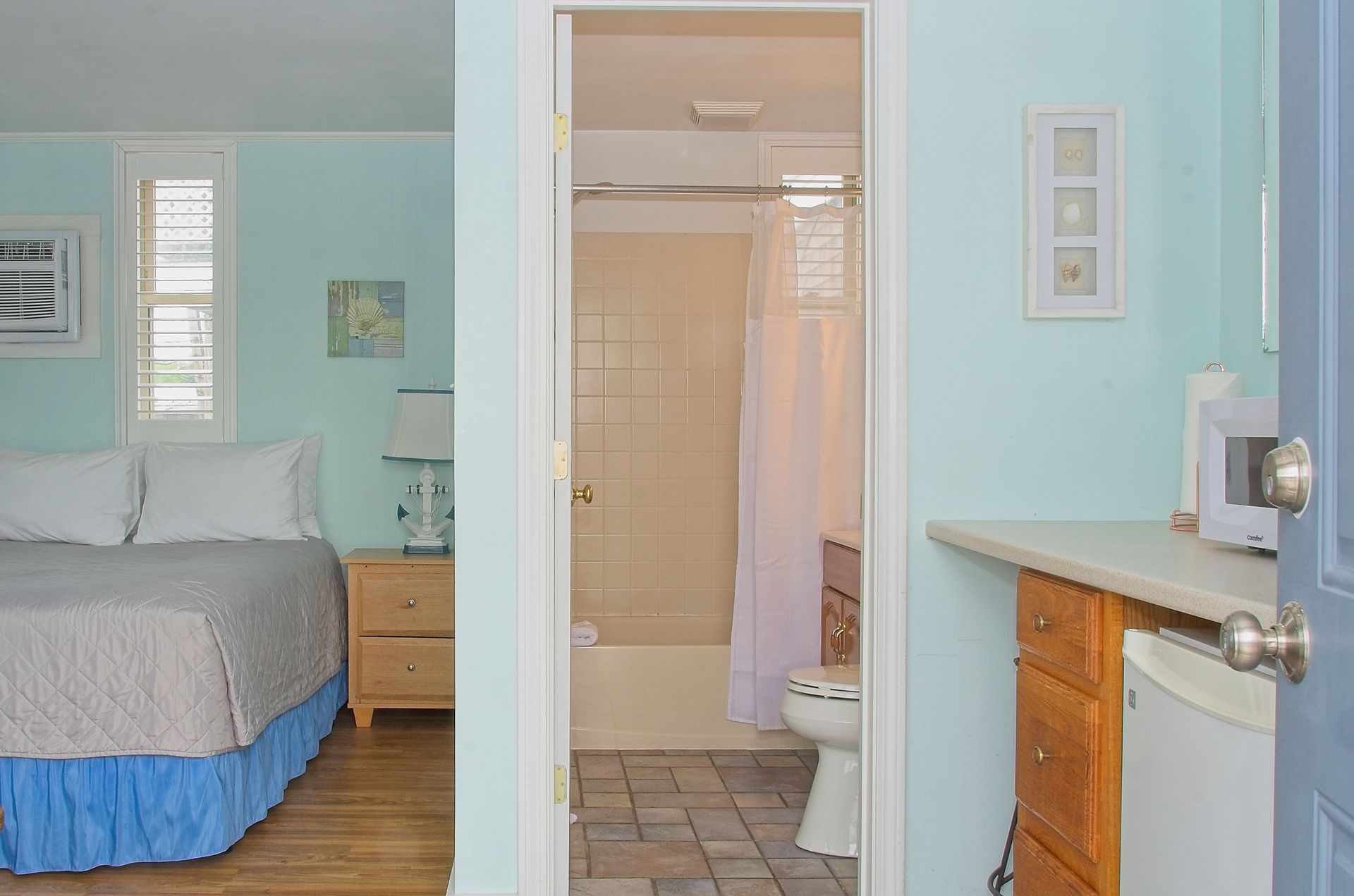 Bedroom with a glimpse of the bathroom through the doorway. Features bed, nightstand, microwave, and pale blue walls.