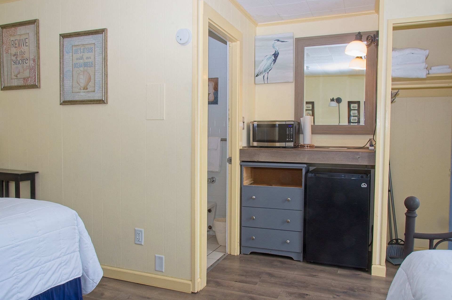 A motel room with two beds, a microwave, mini-fridge, and a bathroom. The walls are light yellow.